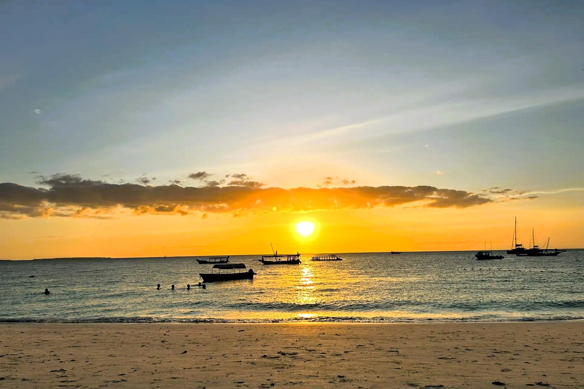 Boats on calm sea beneath an orange sunset