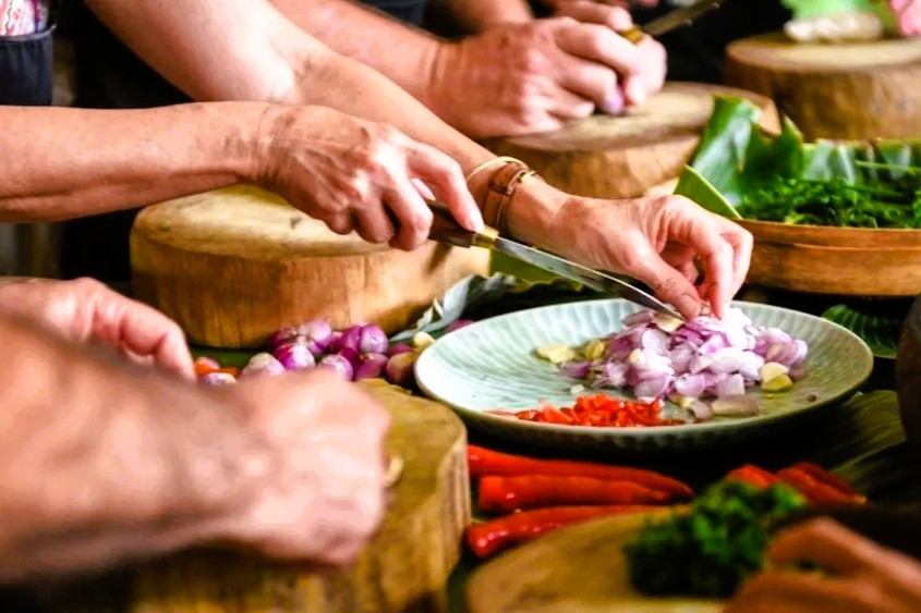 Hands chopping red onion beside fresh vegetables